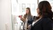 2 women in business attire writing on a whiteboard